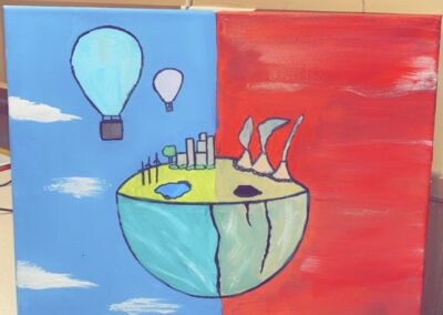 students painting of the earth split in two. One side with a blue cloudy background with hot air balloon's in the sky. this side of the planet also has windmills and trees, the water is clean. the opposite side has a red smokey background with dirty water and exhaust from power plants filling the sky.