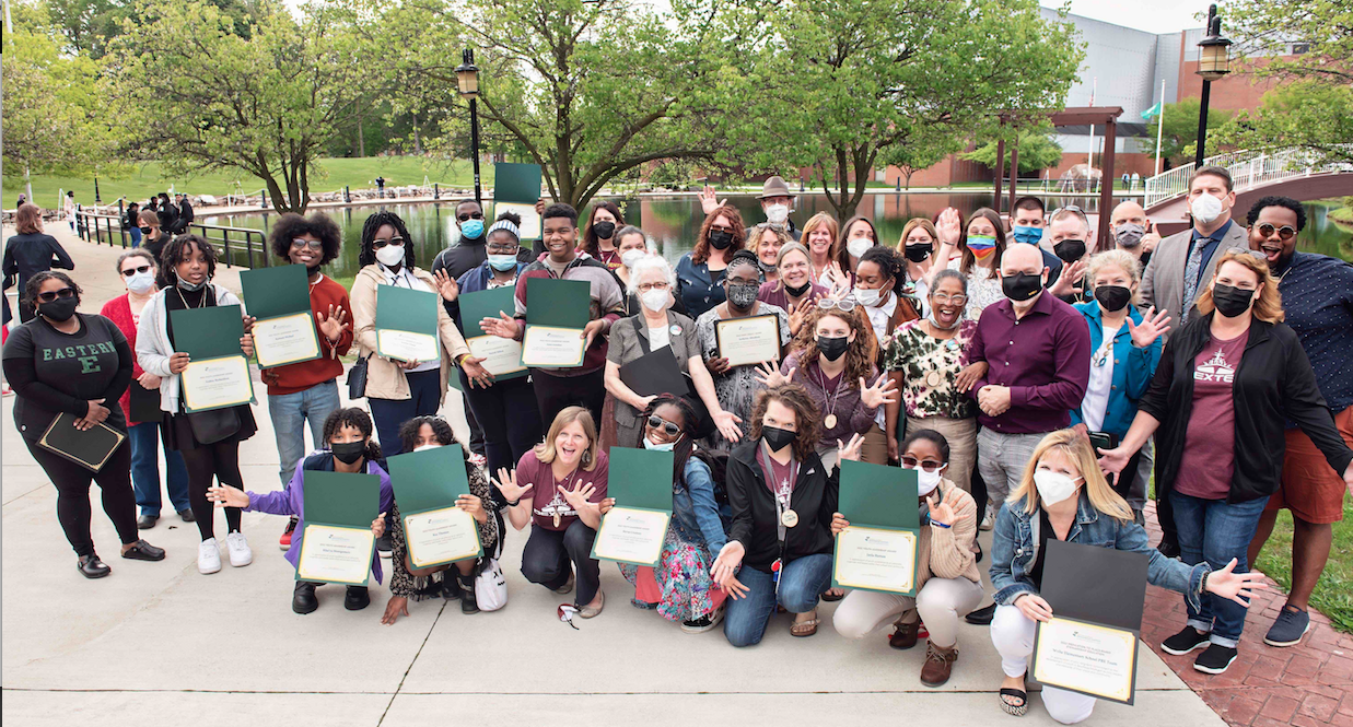 A group shot from the 2022 Community Forum showing all of the folks who won awards and the administrators who supported them.  There are trees in the background and lampposts. Photo credit Leisa Thompson.