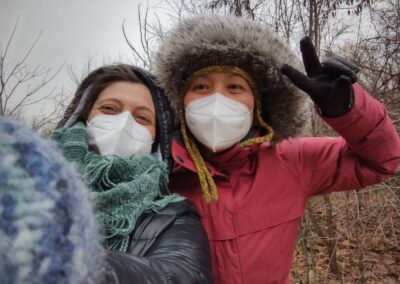 Lisa and Nigora are two of SEMIS staff. This is a photo of them at the Rouge Park during a winter walk for our Coalition members. Nigora is wearing a red jacket with a fur lined hood and Lisa is wearing a black jacket with a hood and a green scarf. they are both masked with smiling eyes.