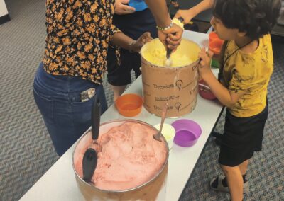 A young person and a person in headscarf are scooping ice cream during the Ice Cream Social